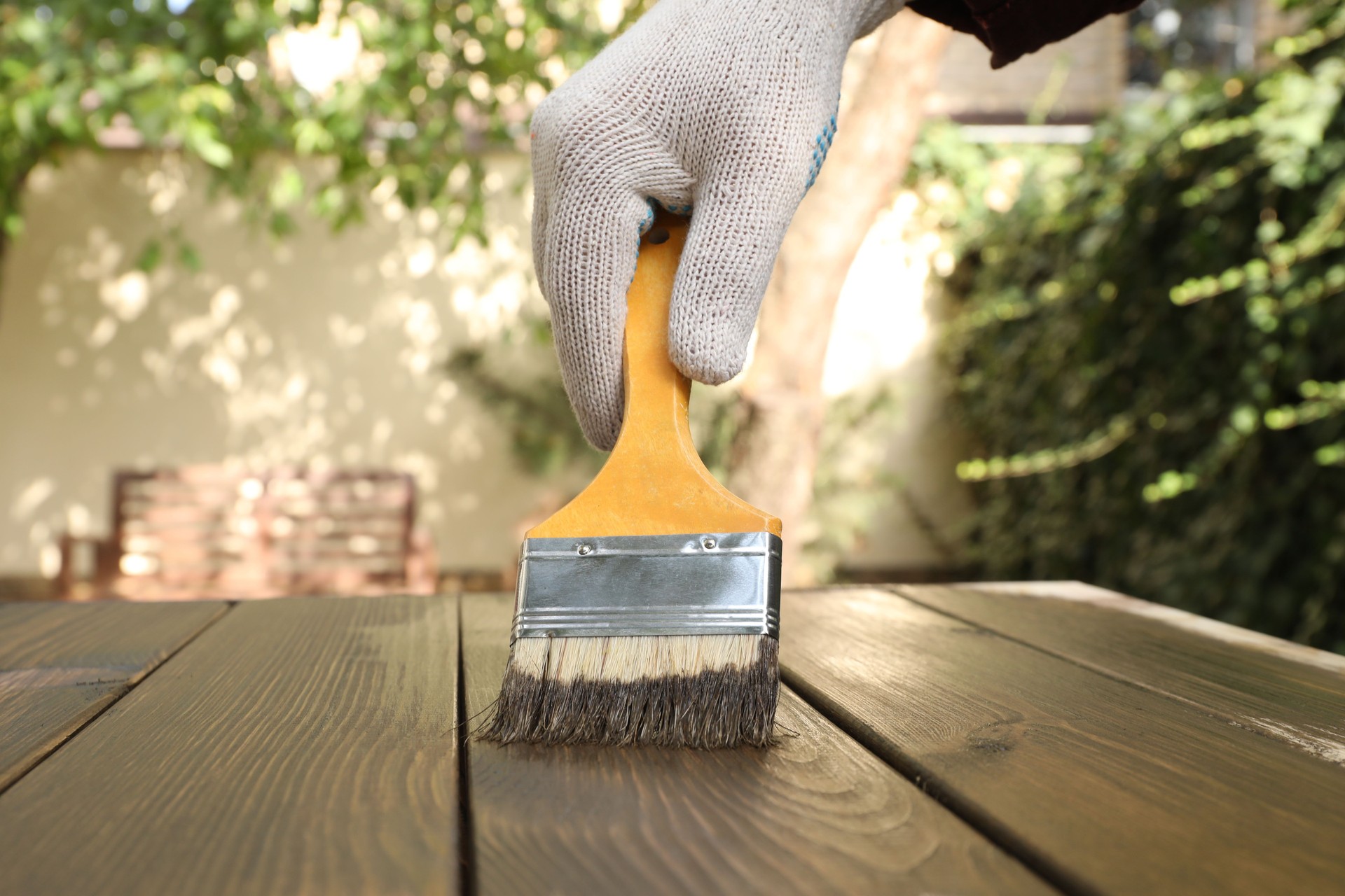 Man applying wood stain onto wooden surface outdoors, closeup